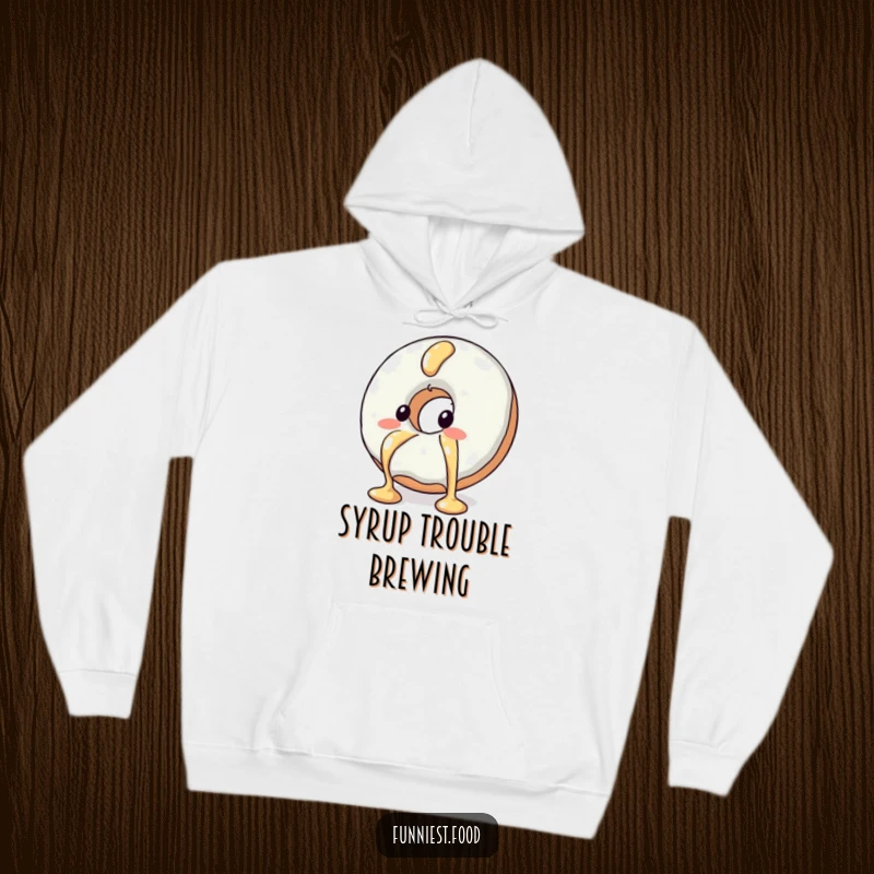 Funny hooded sweatshirt depicting a blushing donut character comically evading a syrup drizzle, combining warmth and humor.